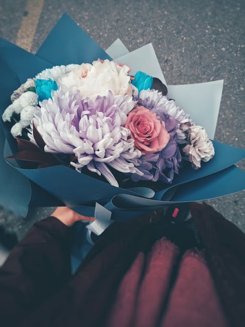 A bridal bouquet featuring a mix of flowers, including large white chrysanthemums with delicate petal textures, soft pink roses with tightly layered petals, and purple lisianthus, all arranged togethe