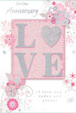 This anniversary card captures the mood of a gentle celebration in Plaistow, with its light, romantic palette and softly textured details. At the heart of the design, the word LOVE appears in raised, glitter-flecked letters, their surfaces shimmering in a mix of blush pink, pearlescent white, and subtle silver accents. The raised print creates a pleasing, tactile relief, as if the word were carefully embossed into the card, inviting a slow, appreciative touch. Beneath it lies a wash of soft pink, glowing just enough to give warmth without stealing focus. Radiating outward from this centre, elegant, stylised flowers and fine, curling vines arc across the card. The blooms are drawn with precise, delicate lines and filled with pale pinks and gentle greys, with tiny hints of silver that suggest foil highlights. Their arrangement resembles a loose floral composition, not rigid or formal, but airy and flowing, much like the romantic bouquets ordered from Flower Delivery Plaistow for anniversaries at local addresses. Little flourishes - small petals, swirling stems, and leaf clusters - add movement, suggesting petals drifting on a breeze. Interspersed among the florals, slender script lettering conveys loving anniversary messages in a graceful, understated style. The lighting appears soft and even, giving the whole card a calm, almost dreamlike presence, like a quiet evening spent together after flowers have been delivered and unwrapped. It feels like a keepsake meant to be treasured, a paper companion to fresh blooms that honours the gentle continuity of a shared life in Plaistow.